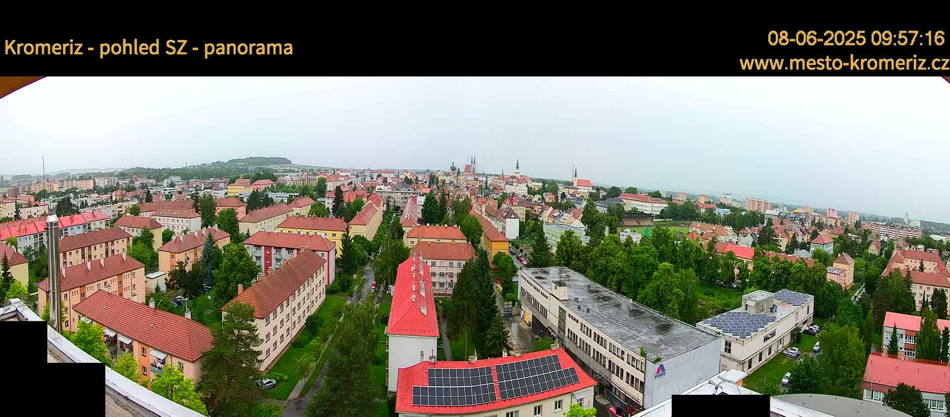 A panoramic view of a town with predominantly red-roofed buildings under an overcast sky.