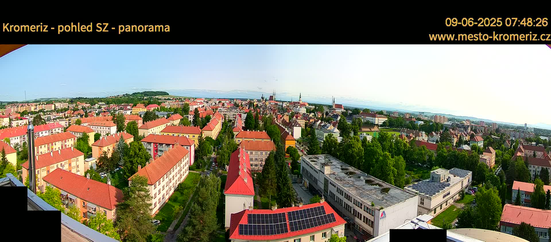 A panoramic view of a town with mostly red-roofed buildings, under a clear sky.