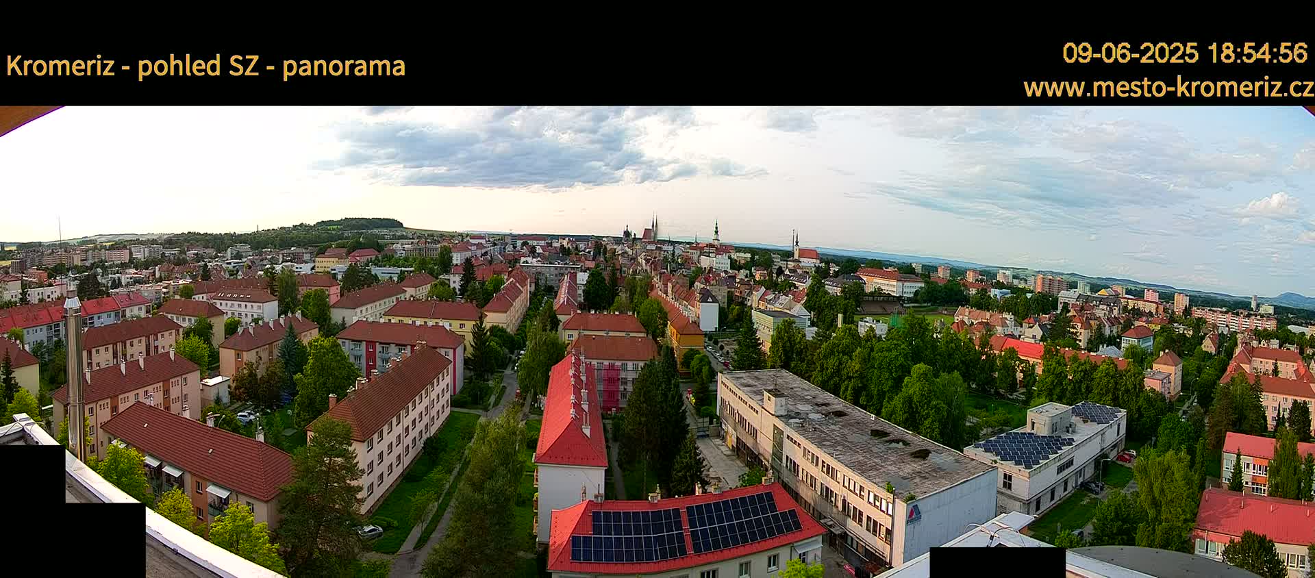 A panoramic view of a town with many red-roofed buildings under a partly cloudy sky.