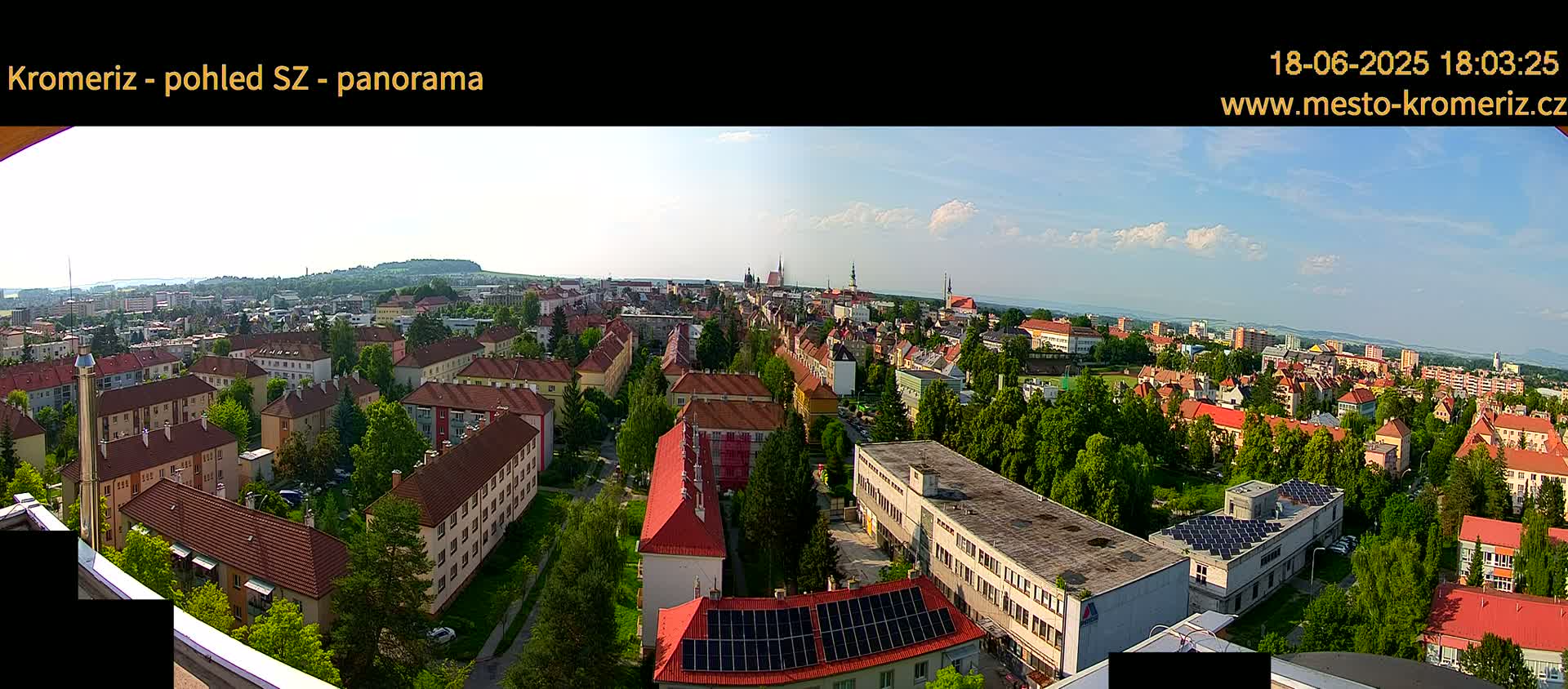 A panoramic view of a town with many low-rise buildings under a partly cloudy, sunny sky.