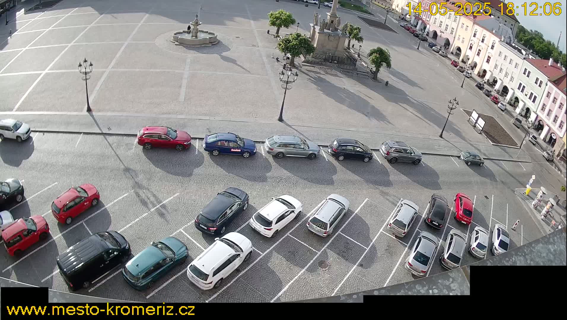 A paved town square with a fountain and several parked cars under sunny conditions.