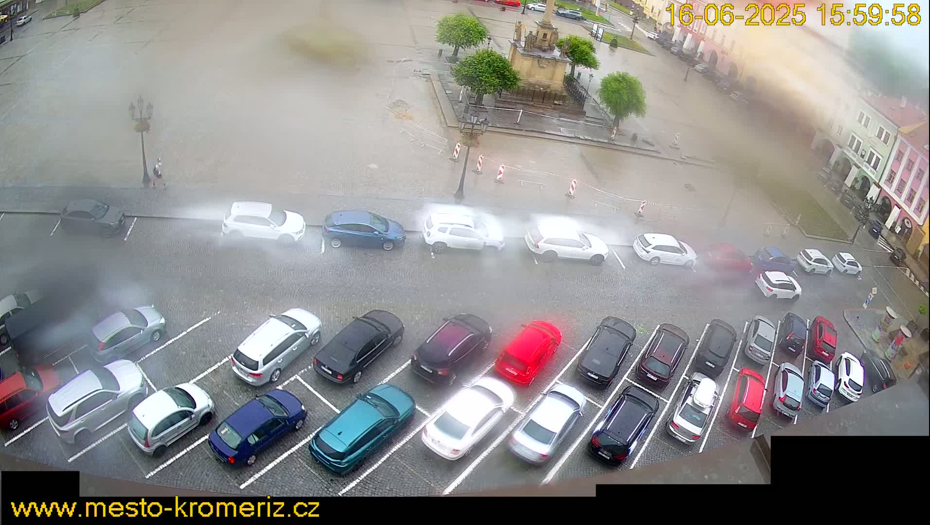 A parking lot filled with cars is seen from an overhead perspective during a heavy rainstorm.