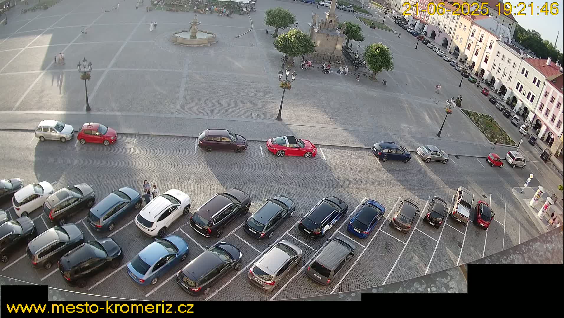 A town square with many cars parked in rows, under sunny daytime conditions.