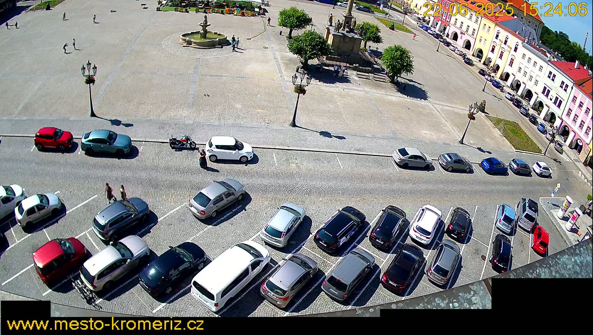 A town square with a fountain and parked cars, under sunny conditions.
