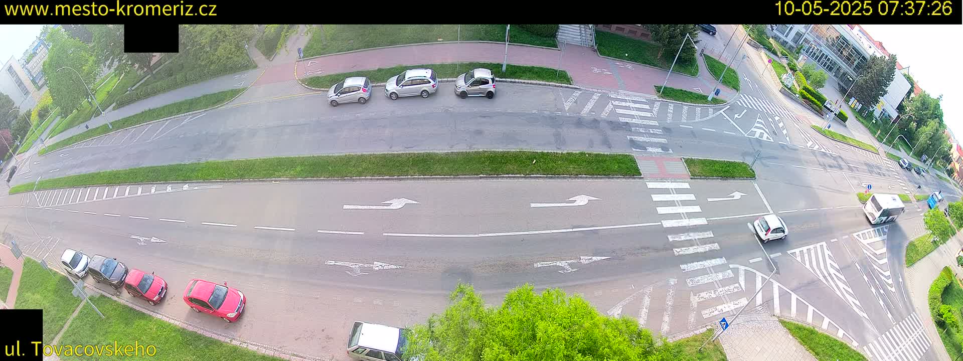 An overhead view of a road intersection with several cars parked and driving on a sunny day.