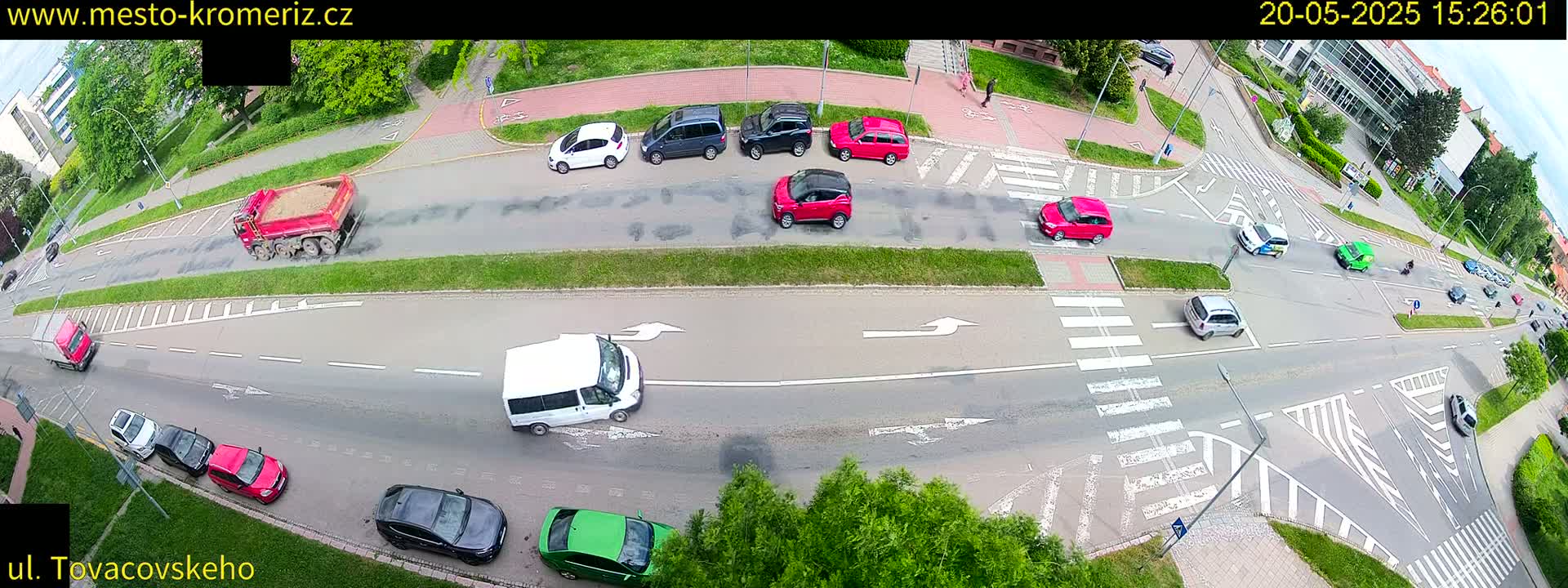 An aerial view of a street intersection with several cars and trucks, on a partly sunny day.