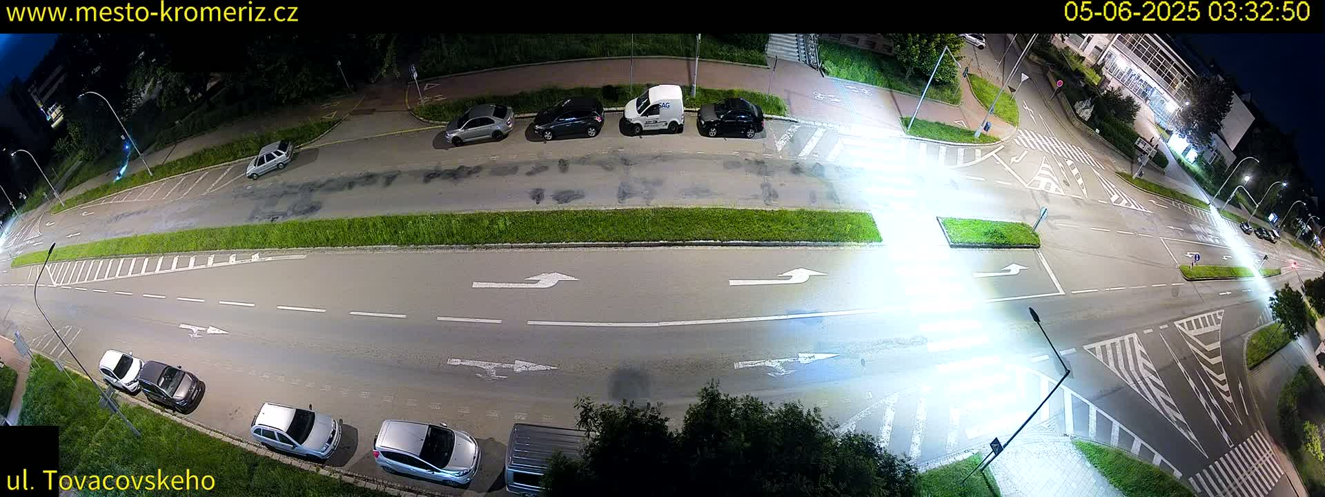 A nighttime, overhead view of a street intersection with several parked and moving cars under bright artificial lights.