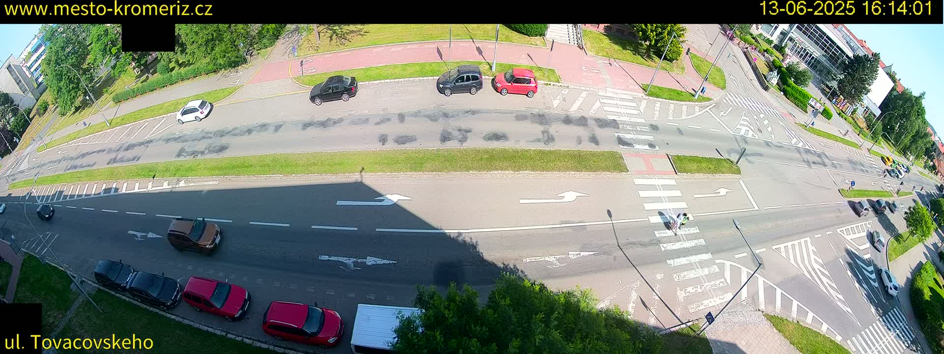A high-angle view of a sunny city street intersection with several cars and a person crossing a pedestrian crossing.