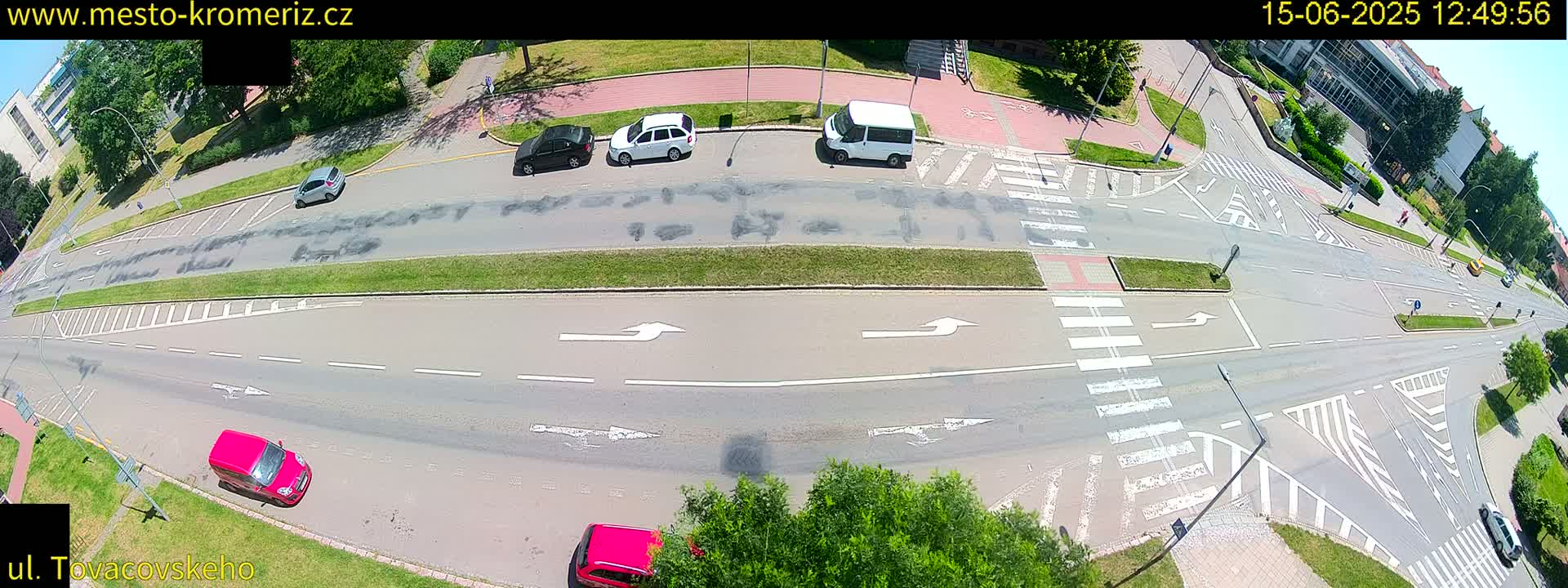 A high-angle view of a multi-lane road intersection on a sunny day, with several cars and a van present.