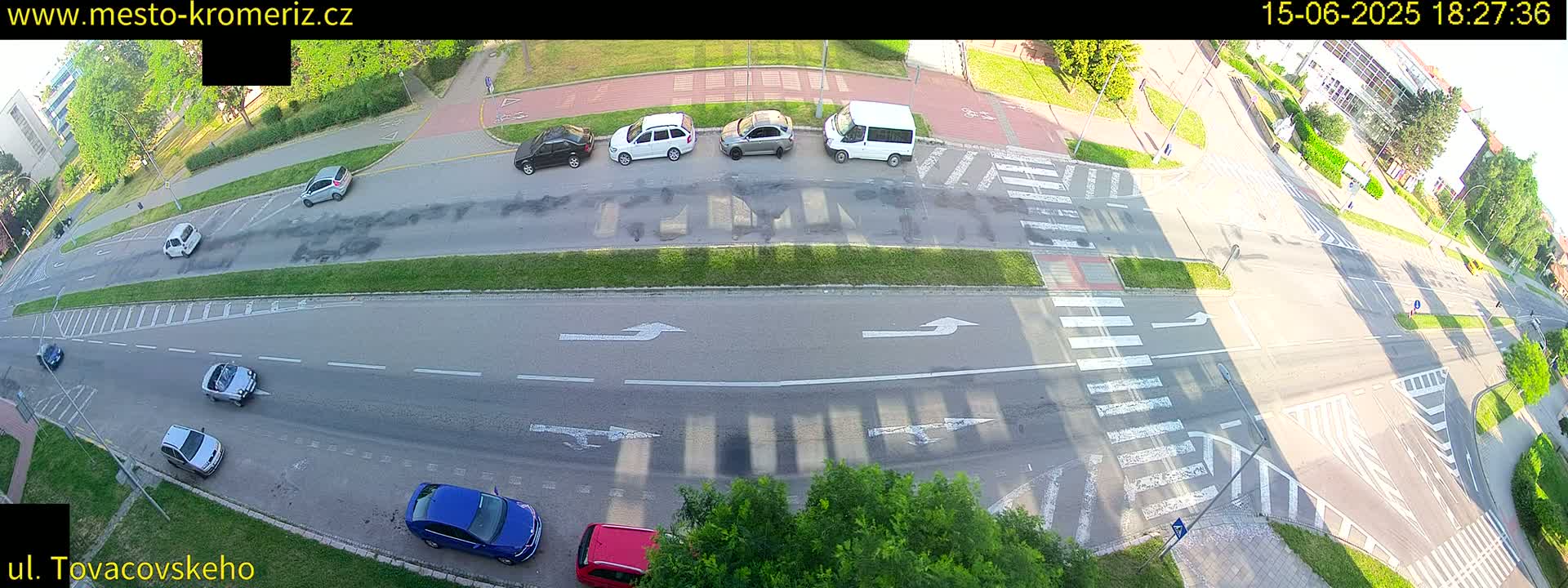 An aerial view shows several cars driving on a multi-lane road with crosswalks and bike lanes under a sunny sky.