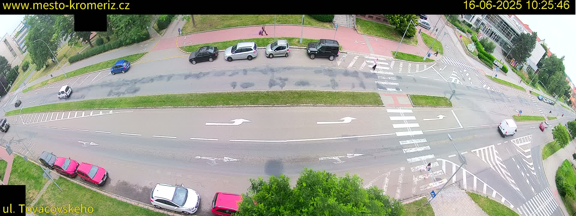 A high-angle view of a street intersection with several cars and pedestrians, under a partly cloudy sky.