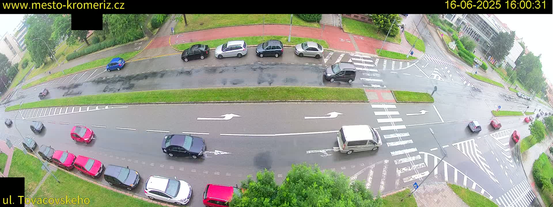 A wet road intersection with numerous cars is viewed from above on a rainy day.