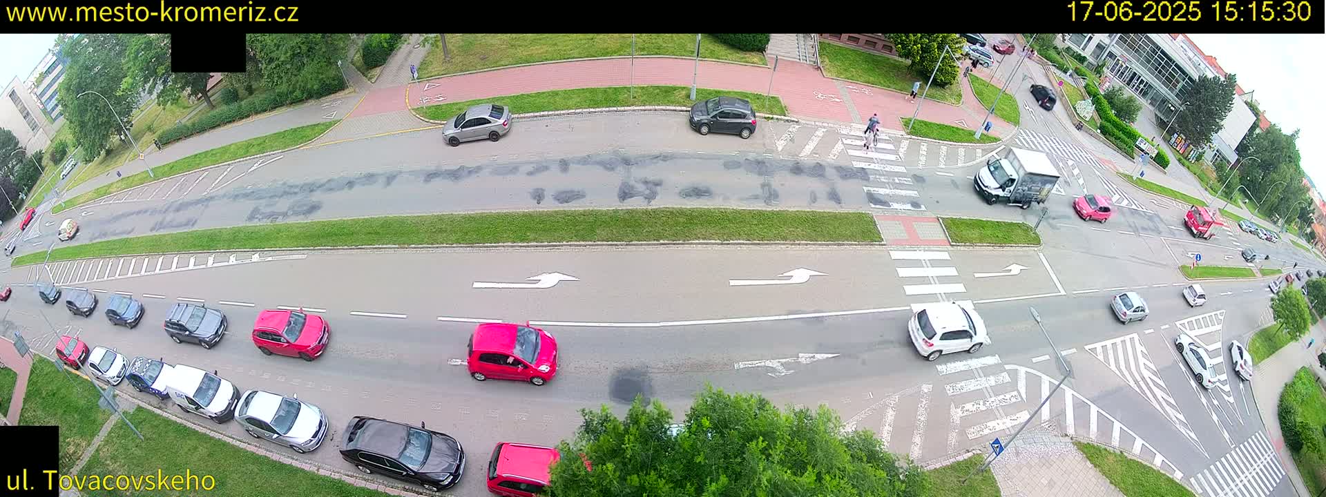 An aerial view of a street intersection with several cars and pedestrians, under sunny conditions.