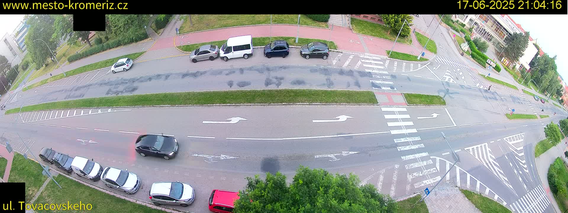 An aerial view of a street intersection at night, showing several cars parked and driving on a roadway with crosswalks and bike lanes, under partly cloudy skies.