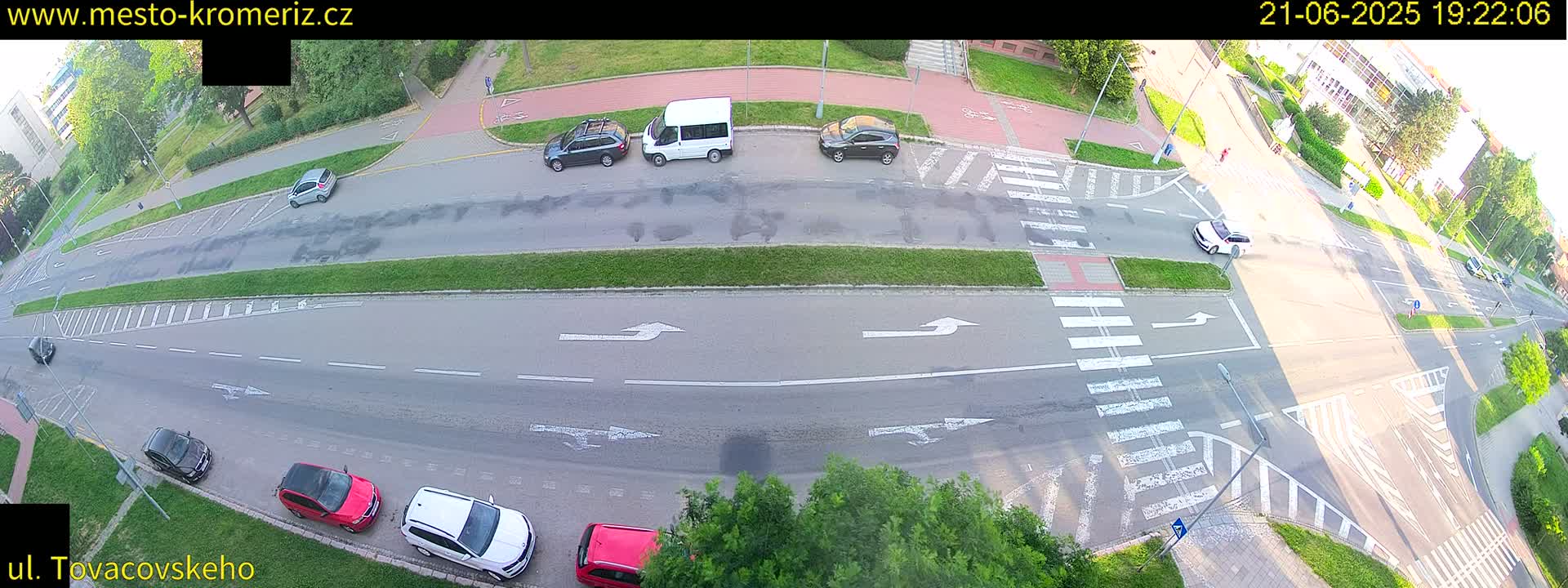 An aerial view of a road intersection with several cars parked and driving on a sunny day.