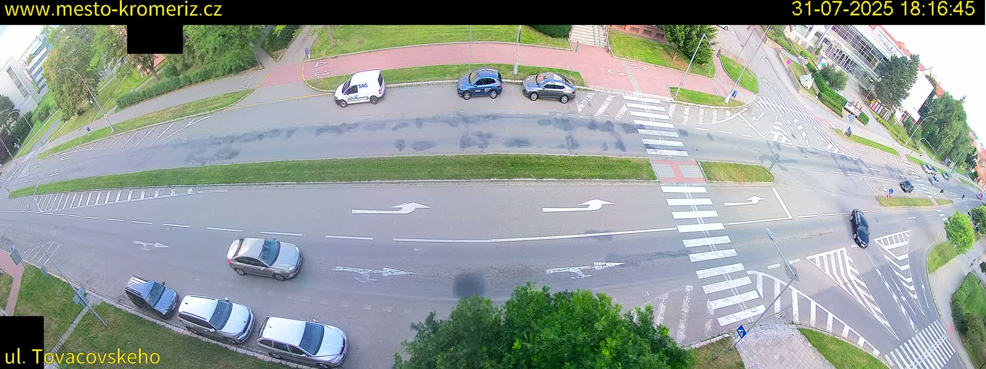 An aerial view of a road intersection with several cars parked and driving, under partly cloudy daytime conditions.