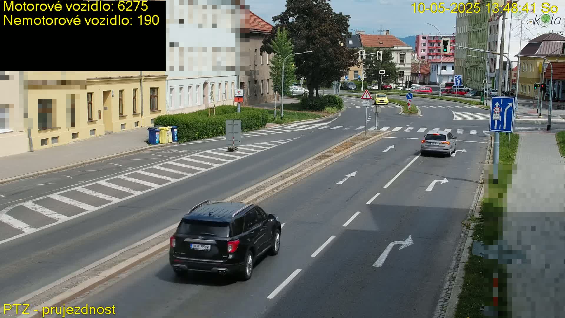 A sunny day reveals a street intersection with several cars, including a dark SUV and a light-colored hatchback, navigating the roadway.