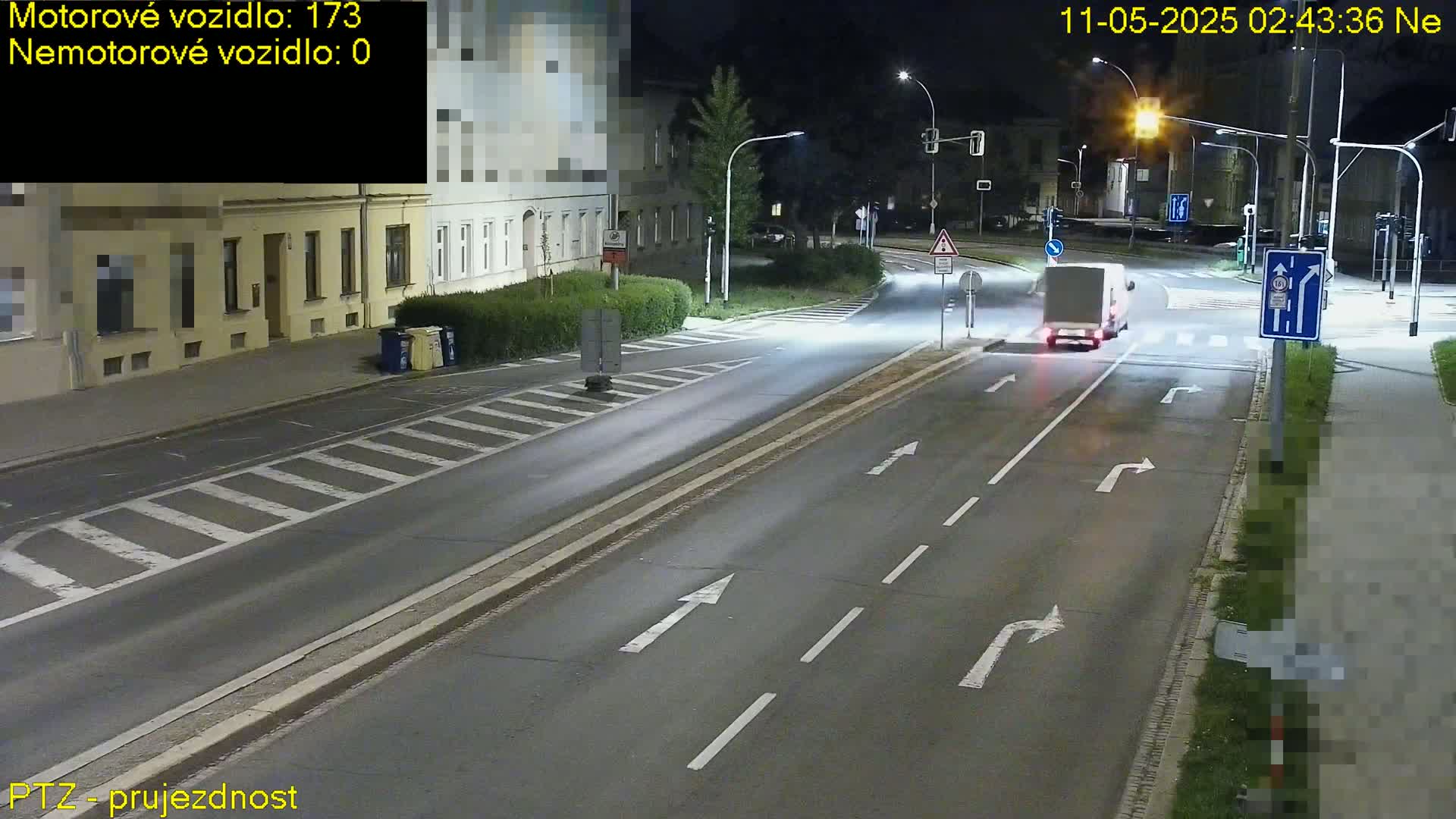 A white van drives on a dark, multi-lane road at night, past buildings with streetlights illuminating the scene.