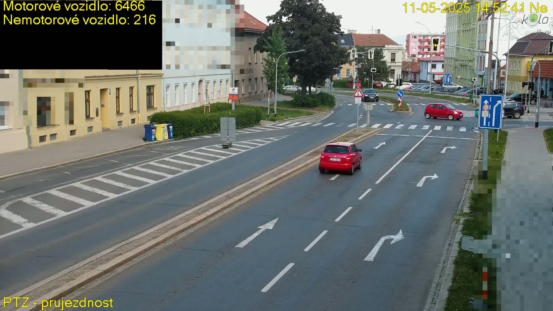 Two red cars and several other vehicles are driving on a multi-lane road near a pedestrian crossing under a partly cloudy sky.