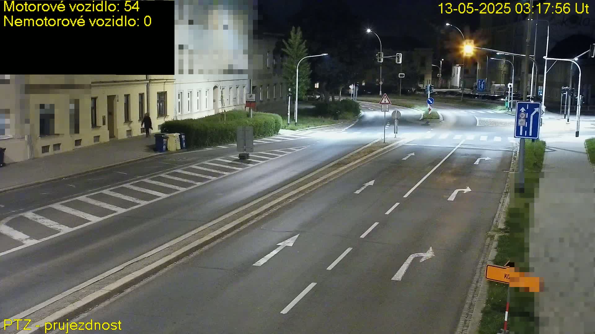 A nighttime street scene shows a multi-lane road with white lane markings, streetlights, and a pedestrian walking near buildings.