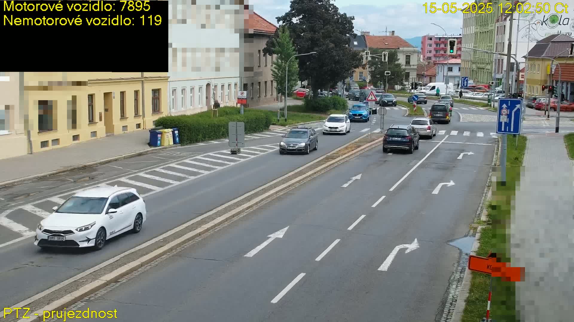 Several cars are driving on a multi-lane road in front of buildings on an overcast day.