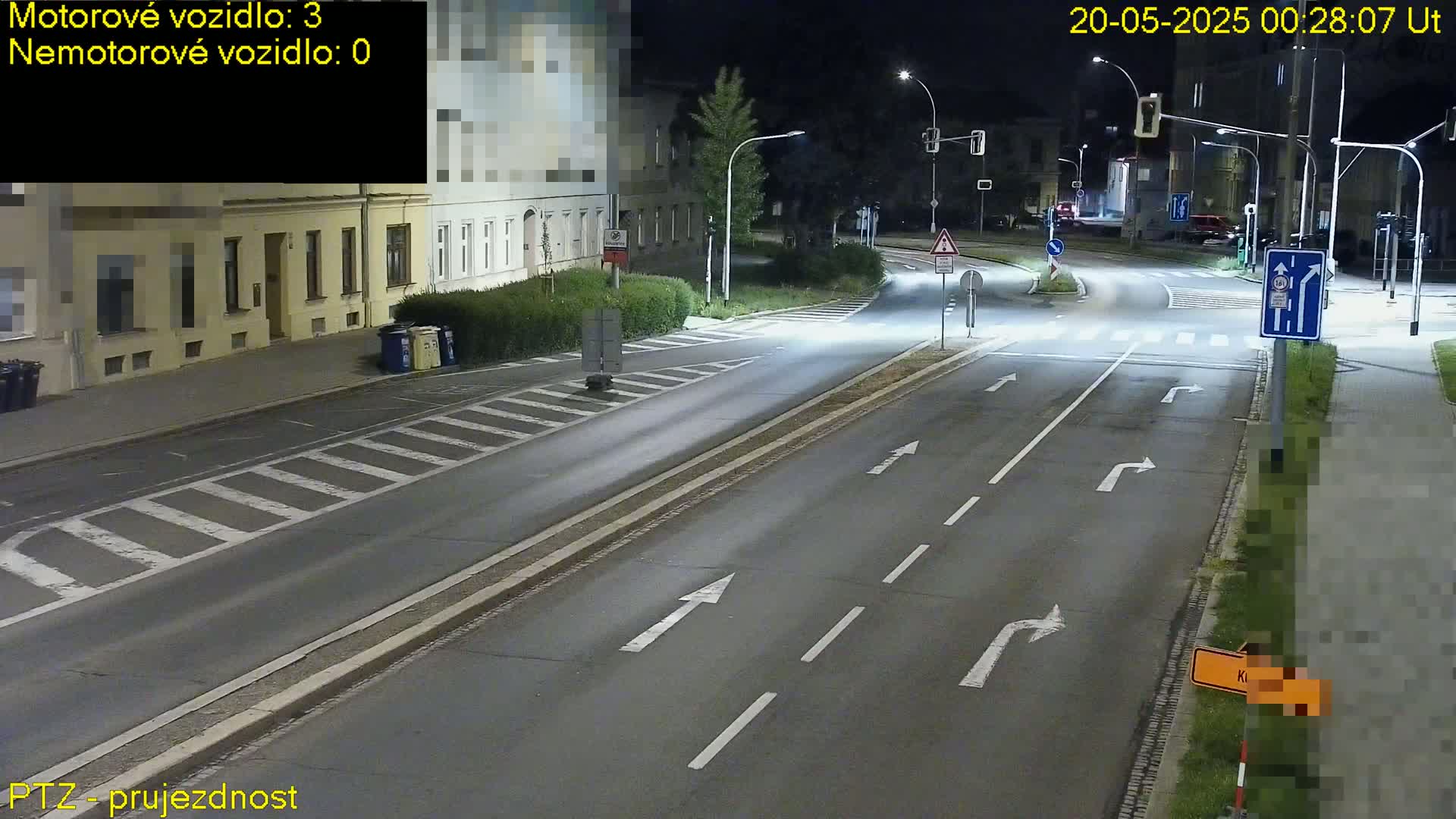 A nighttime street intersection with several streetlights illuminating a mostly empty road, showing lane markings and traffic signs.