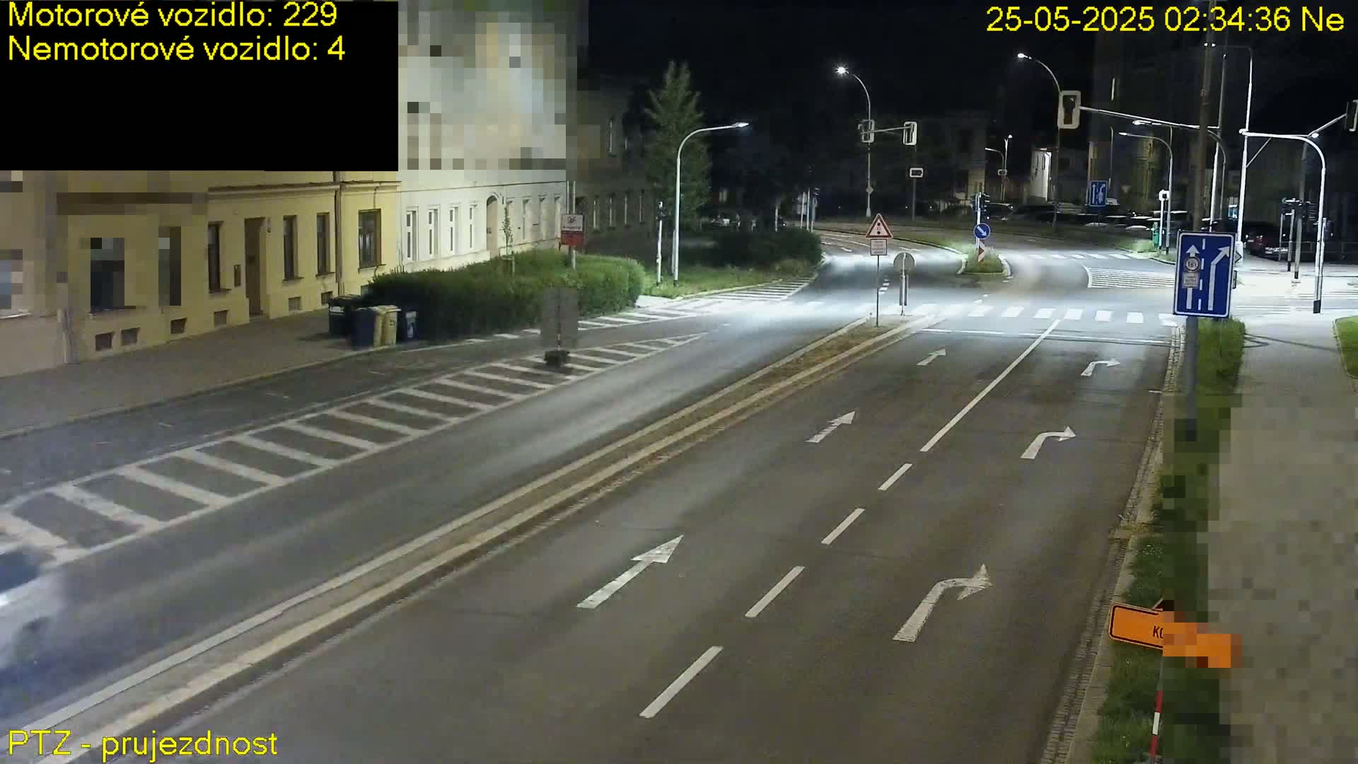 A nighttime view of a multi-lane road intersection with streetlights illuminating buildings and a pedestrian crossing.
