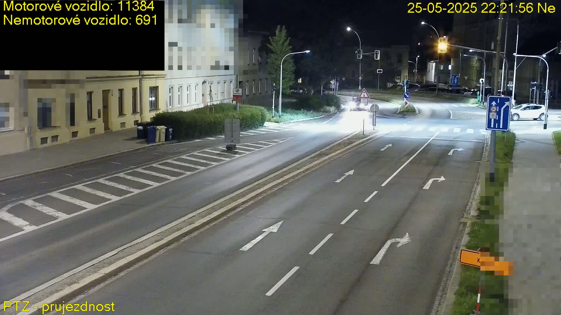A nighttime street scene shows a multi-lane road with traffic and streetlights,  alongside buildings and pedestrian crossings.