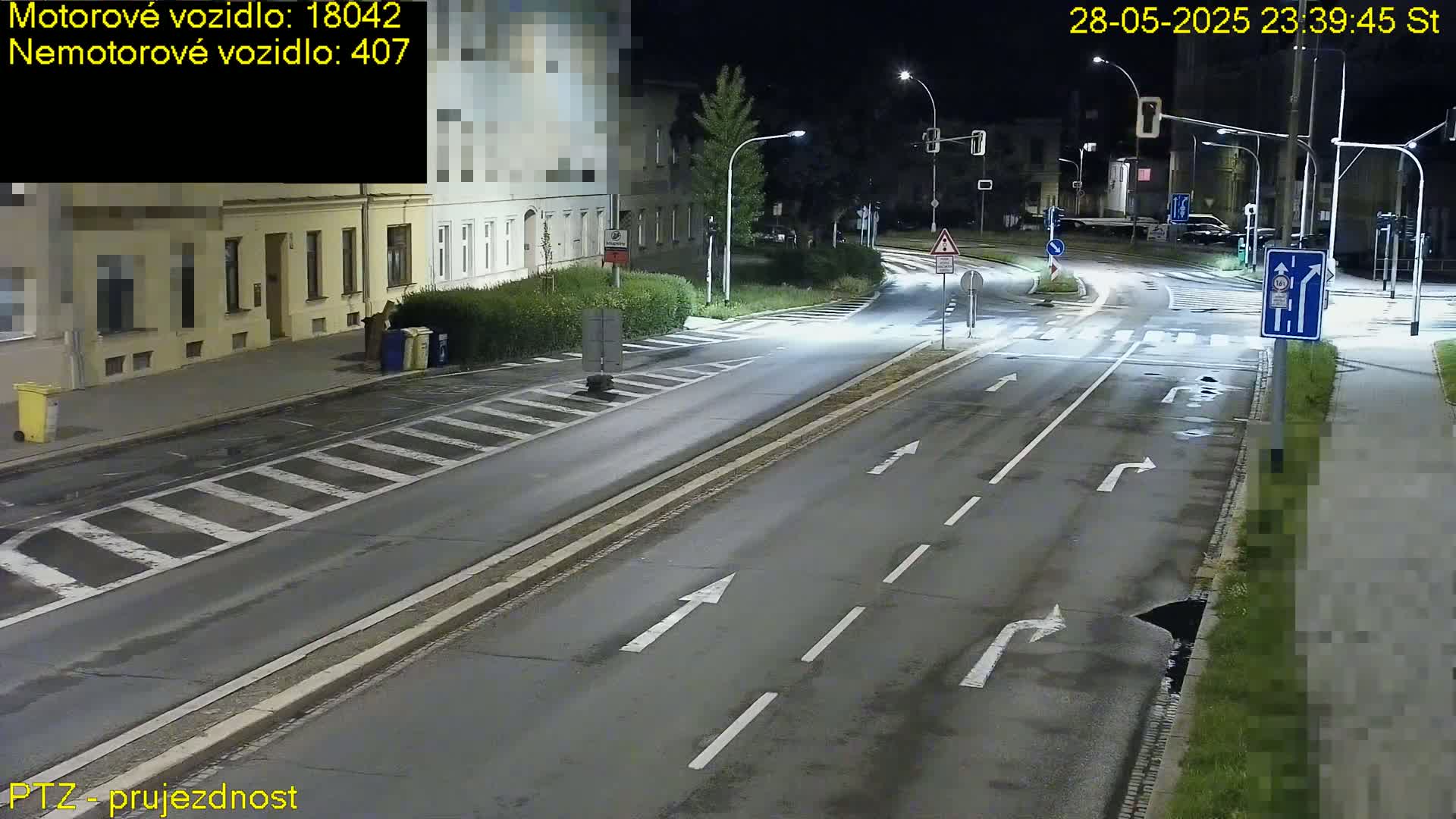 A nighttime view of a multi-lane road intersection with streetlights illuminating the asphalt and nearby buildings.