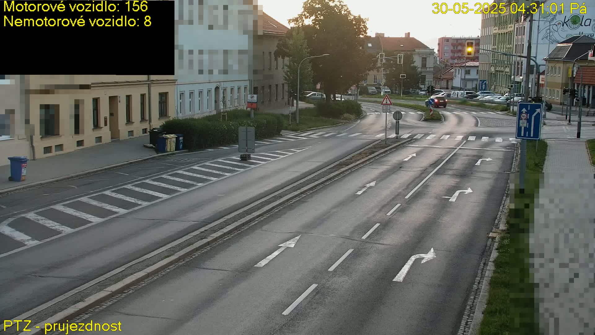 A mostly empty road intersection with light traffic under a partly sunny sky at dawn.