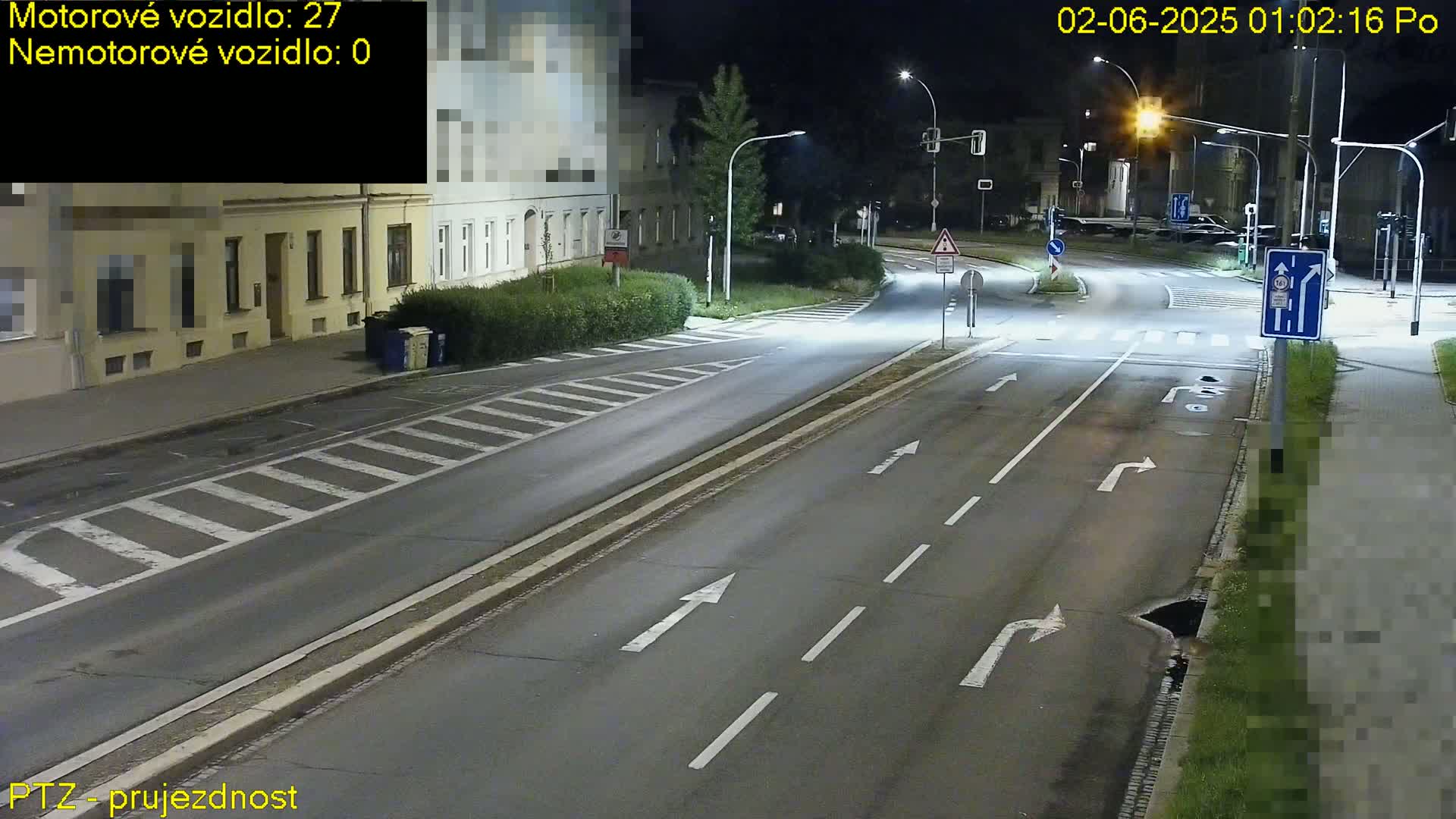 A nighttime street scene shows a multi-lane road with painted lane markings and streetlights illuminating an intersection near buildings.