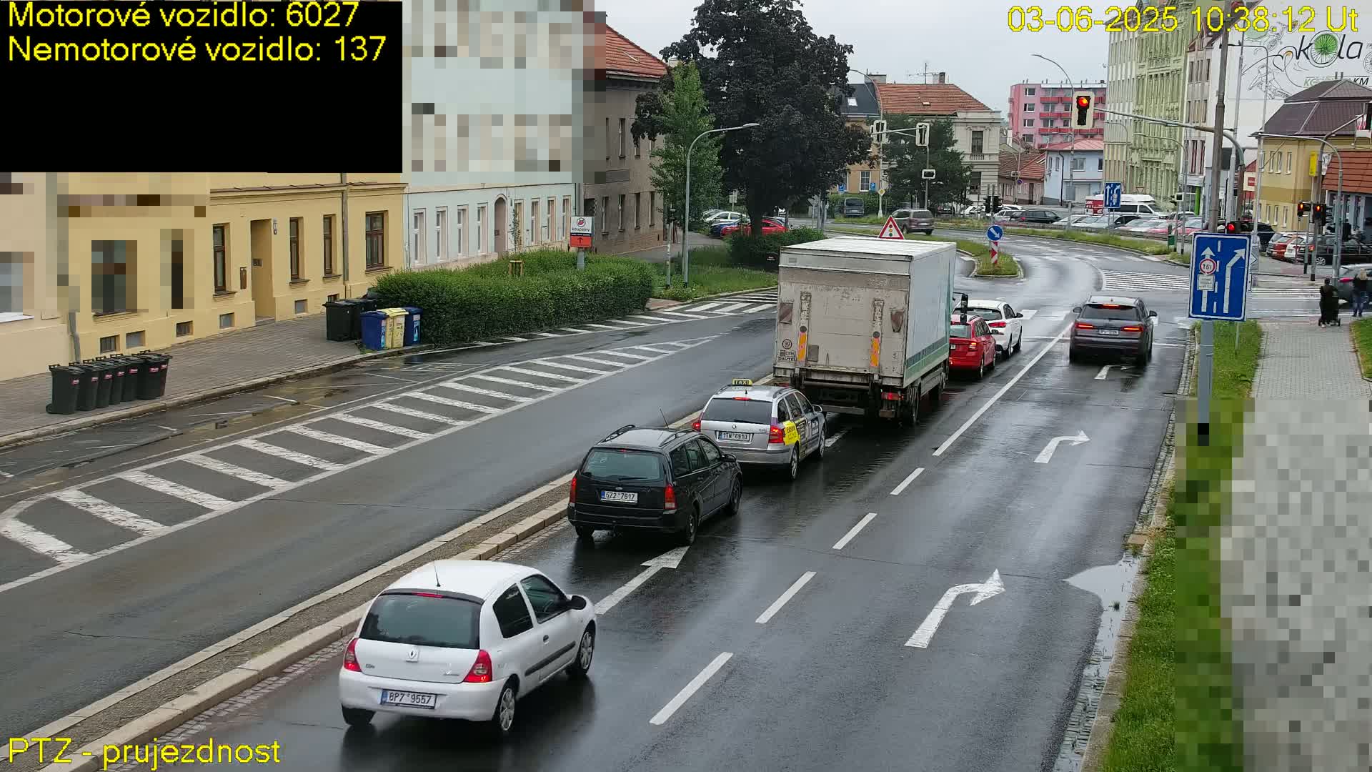 Several cars and a large truck are driving on a rain-slicked street in front of buildings.