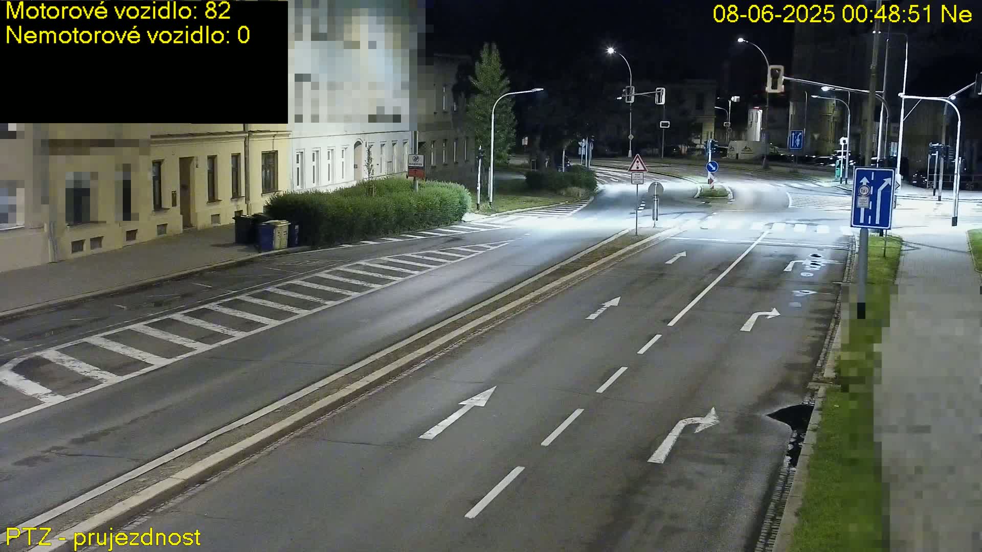 A nighttime street scene shows a multi-lane road with directional arrows painted on the asphalt, and buildings and streetlights lining the road.