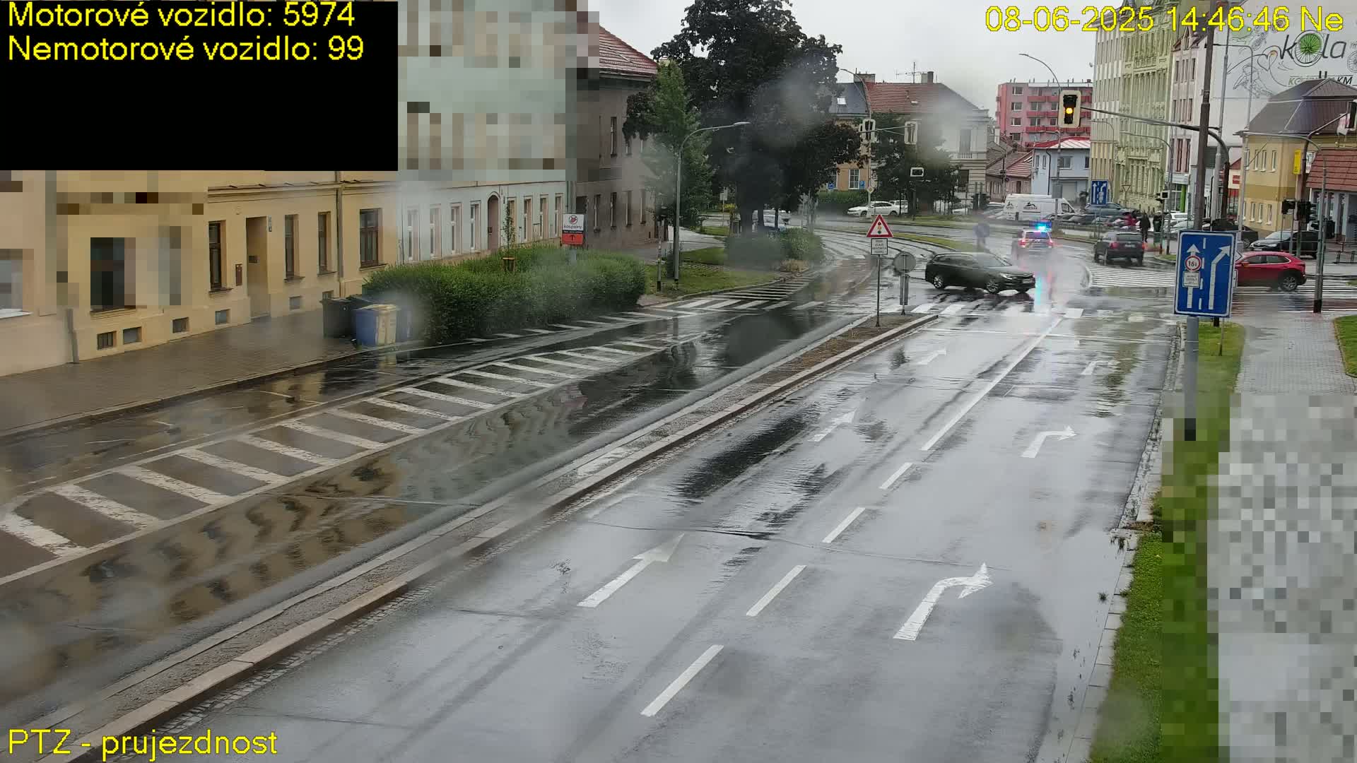 A wet, rainy street scene shows several vehicles at a crossroad in front of buildings.