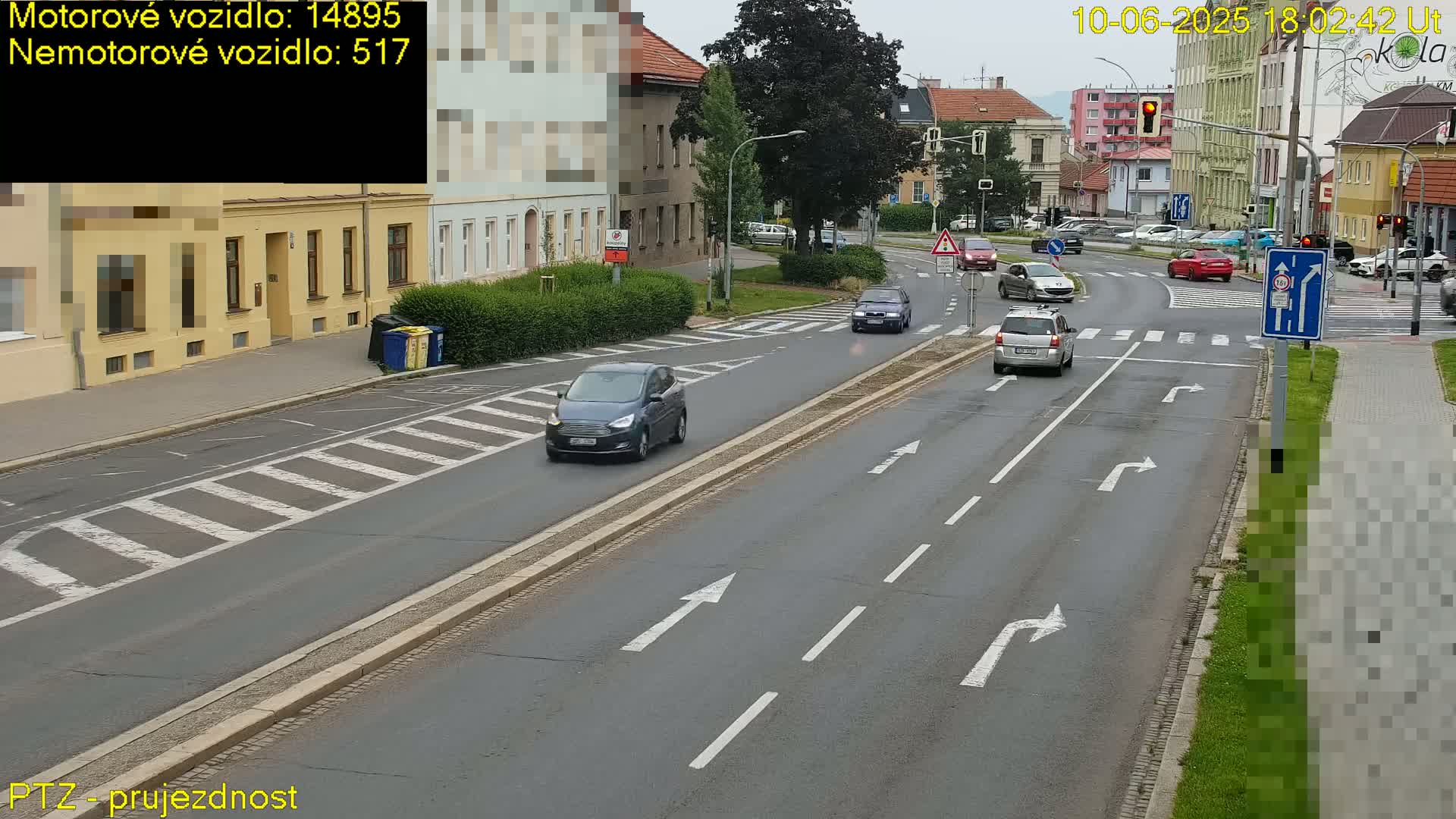 Several cars are driving on a multi-lane road with pedestrian crossings under overcast skies.