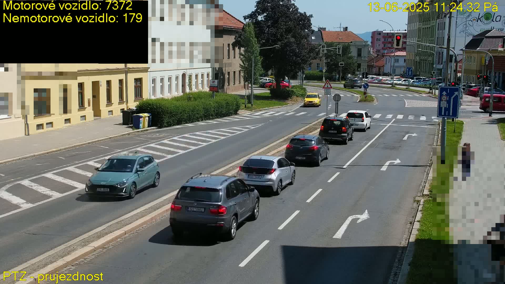 Several cars are driving on a sunny city street with a pedestrian crossing and a person walking on the sidewalk.