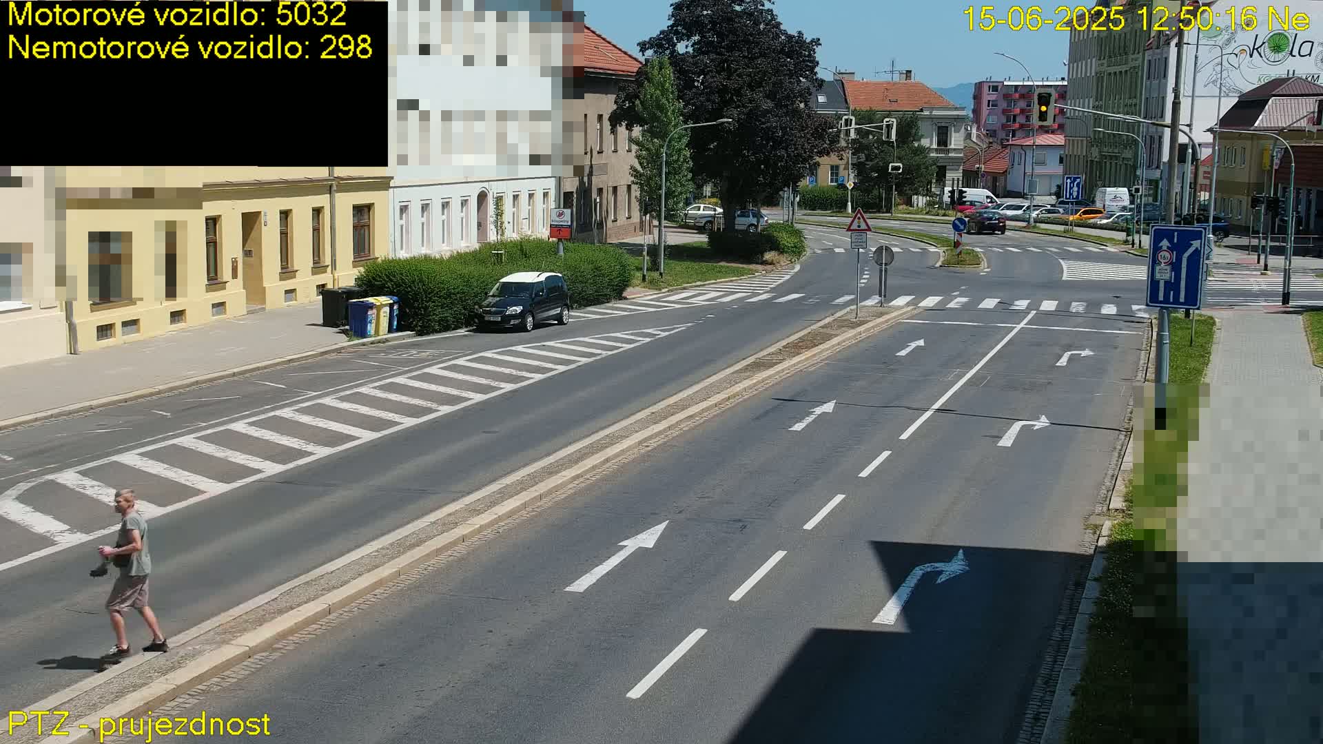 A person walks along a sunny city street with several cars visible at a crossroads.