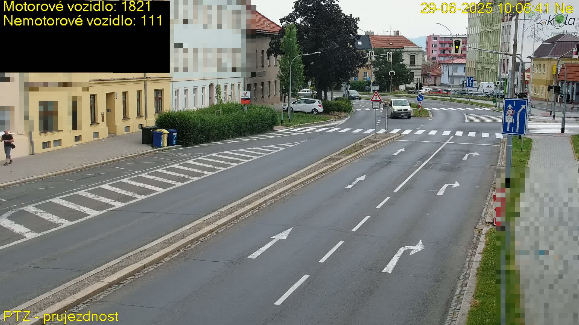 A wet street scene shows a multi-lane road with pedestrian crossings, several cars, and a person walking on the sidewalk.