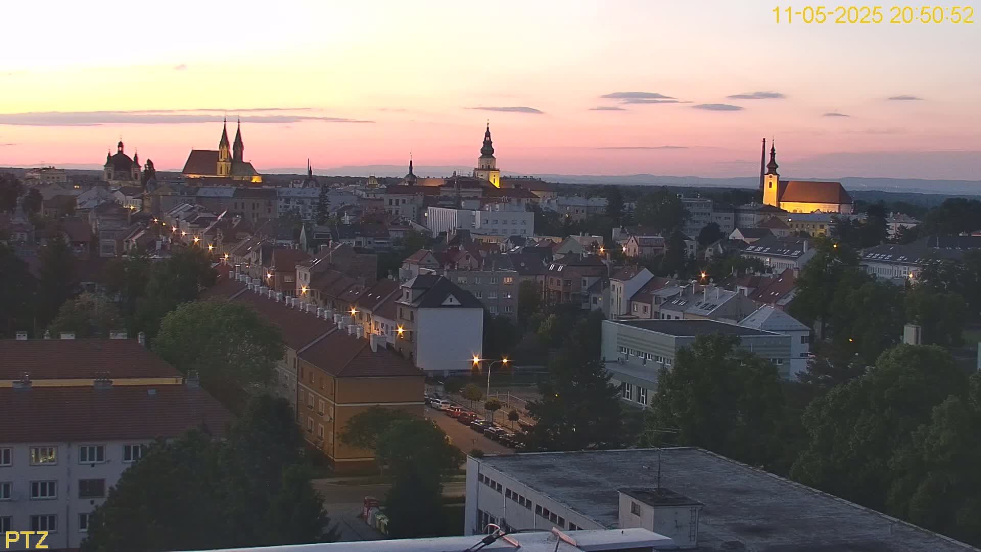 A pink sunset illuminates a cityscape of closely-packed buildings and several prominent church steeples.