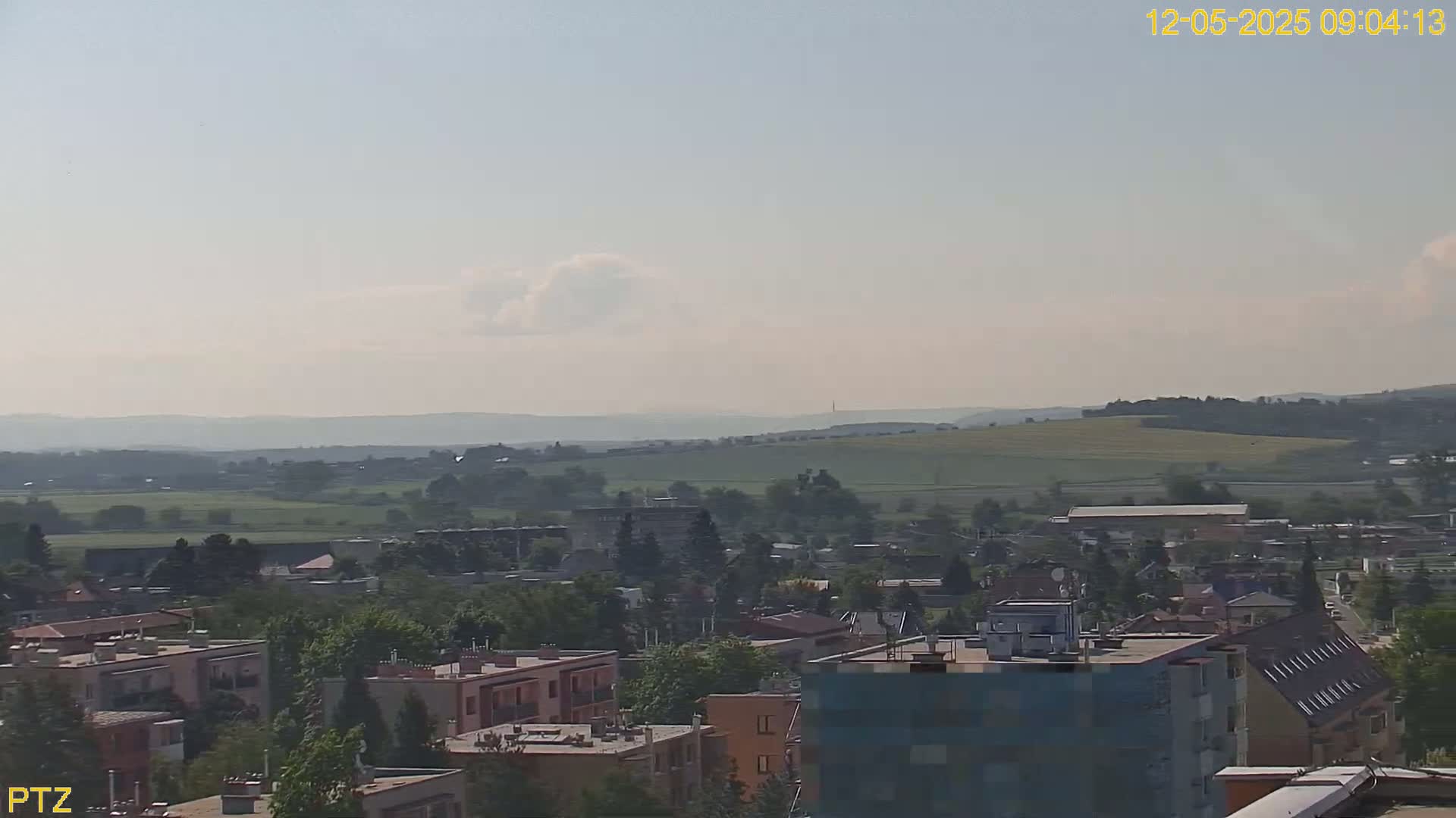 A hazy, sunny day overlooks a town nestled in a valley surrounded by rolling green hills.