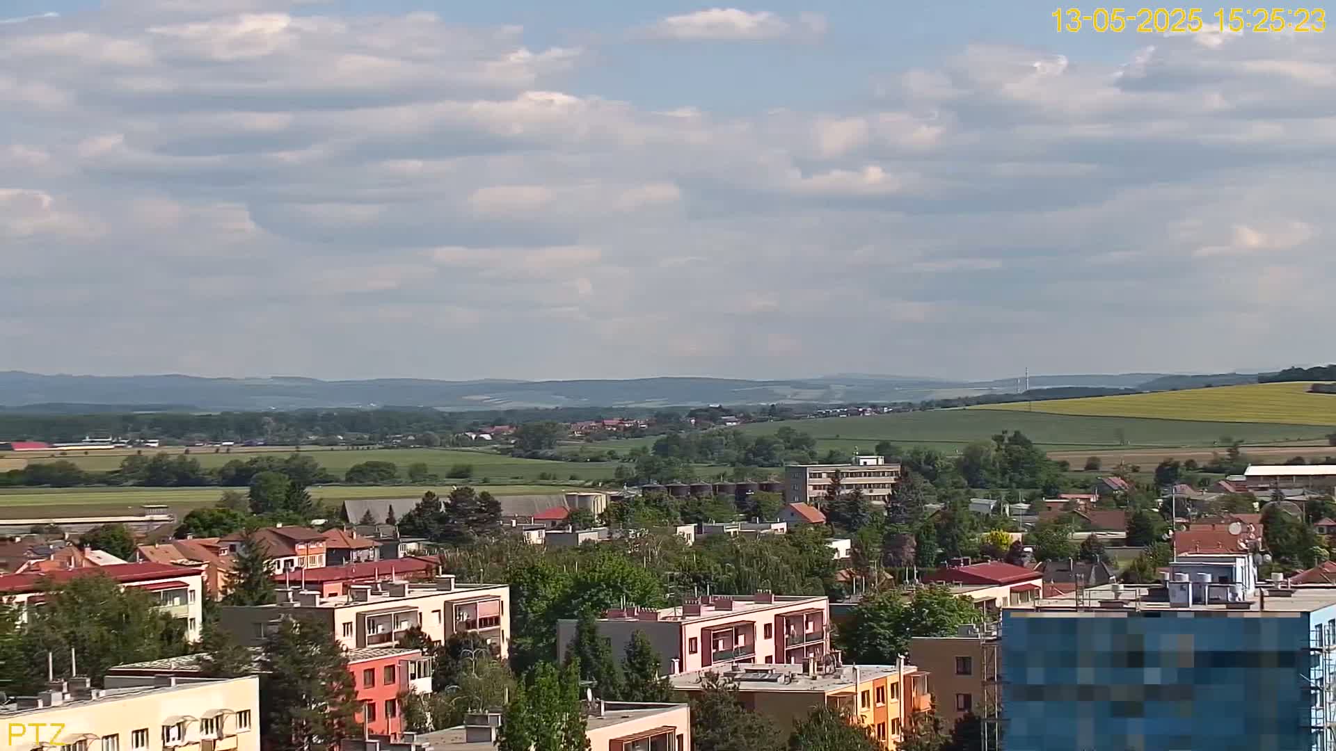 A partly cloudy day reveals a sprawling town nestled in a valley, surrounded by rolling hills and fields.