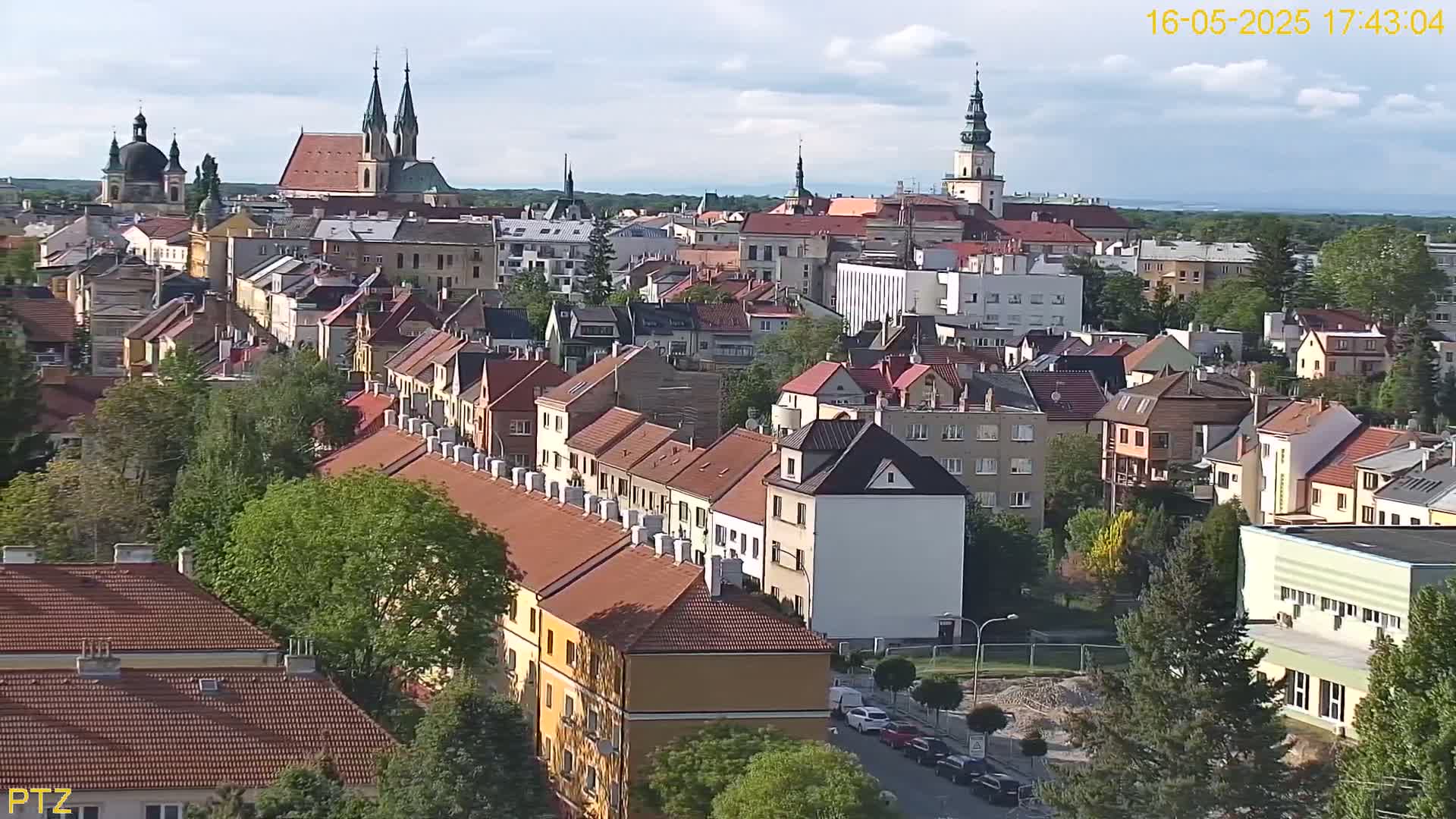 A partly cloudy day reveals a cityscape of many red-roofed buildings, with several church steeples prominent in the distance.