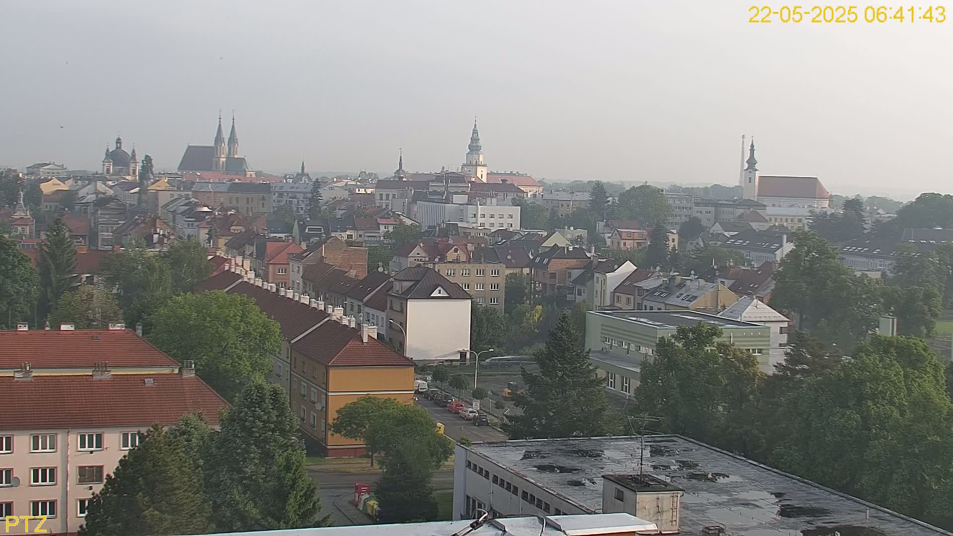 A hazy, aerial view of a town with numerous buildings, churches, and green trees.