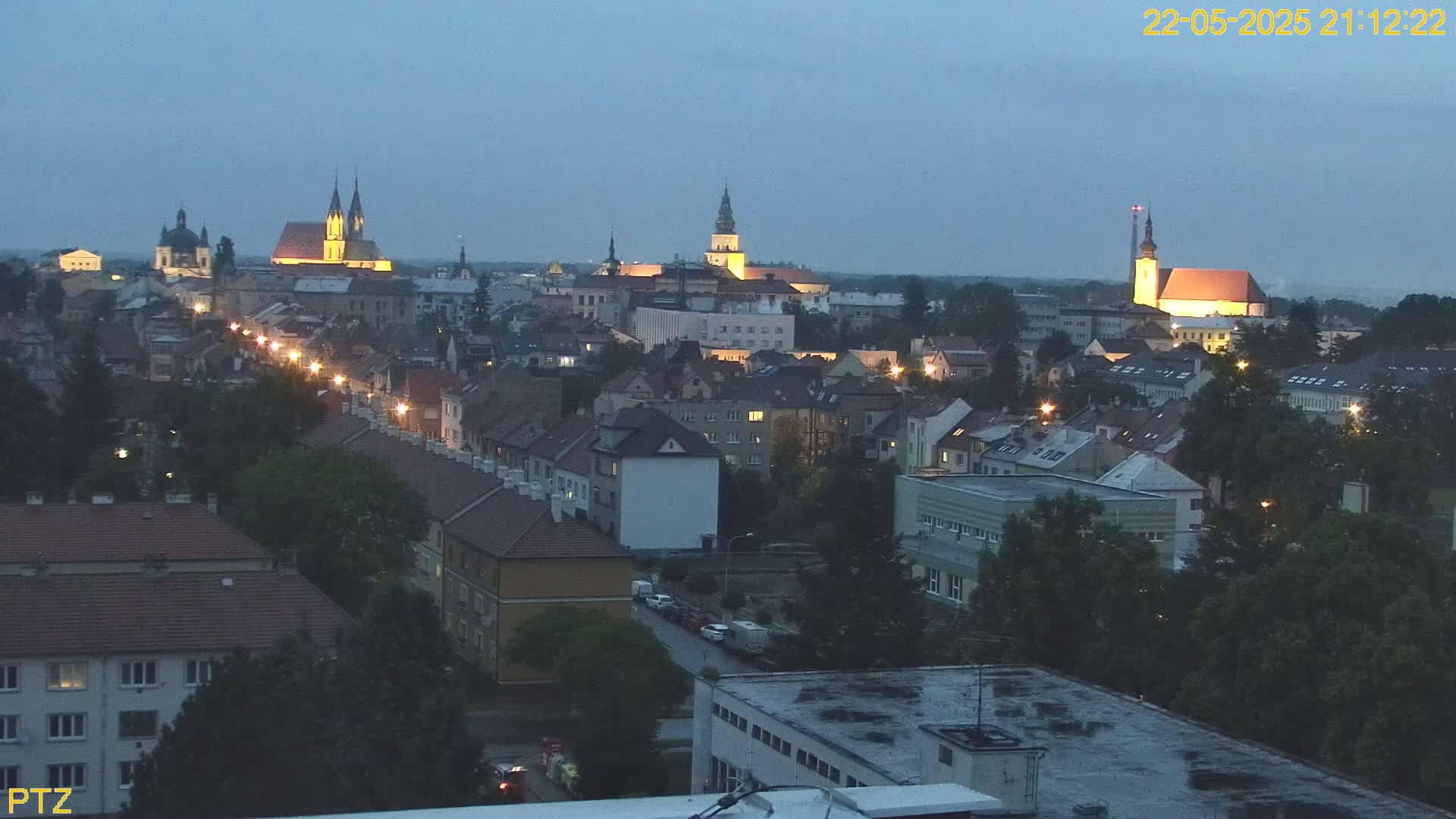 A nighttime, high-angle view of a town illuminated by streetlights, featuring several prominent church spires and a cityscape of buildings under a twilight sky.