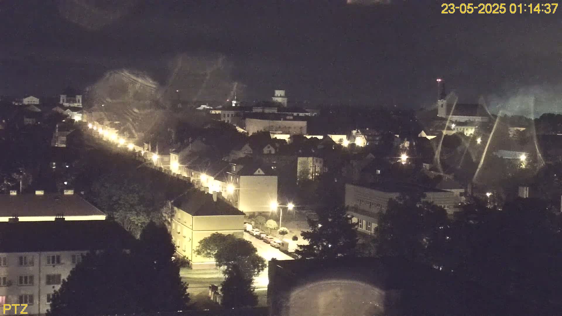 A nighttime, high-angle view of a town with illuminated streets and buildings, under a mostly clear sky.