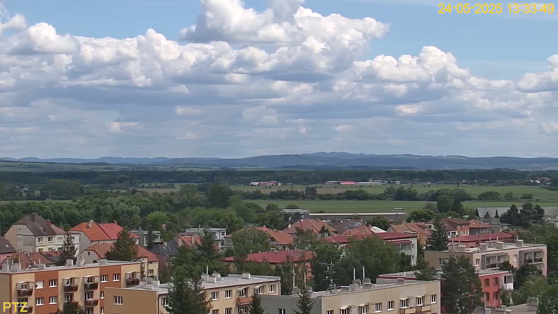 A partly cloudy day reveals a sprawling residential area nestled in a verdant valley, with distant hills visible on the horizon.