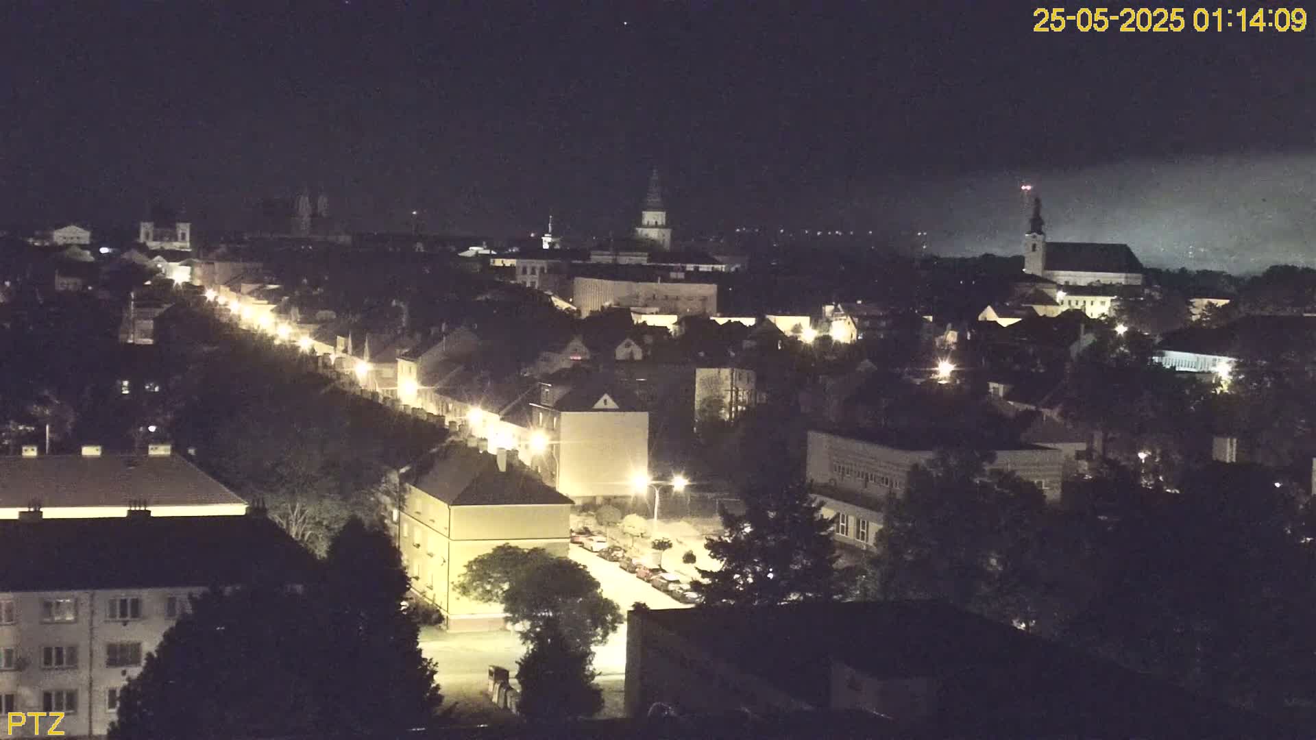 A nighttime, high-angle view of a town with a brightly lit street running through its center, under a clear, dark sky.