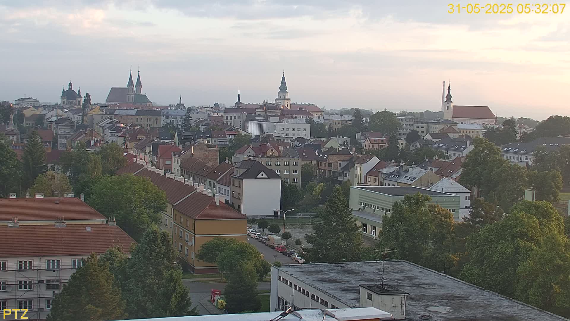 An elevated view of a European city on a hazy, overcast morning, showing many low-rise buildings and several church steeples in the distance.