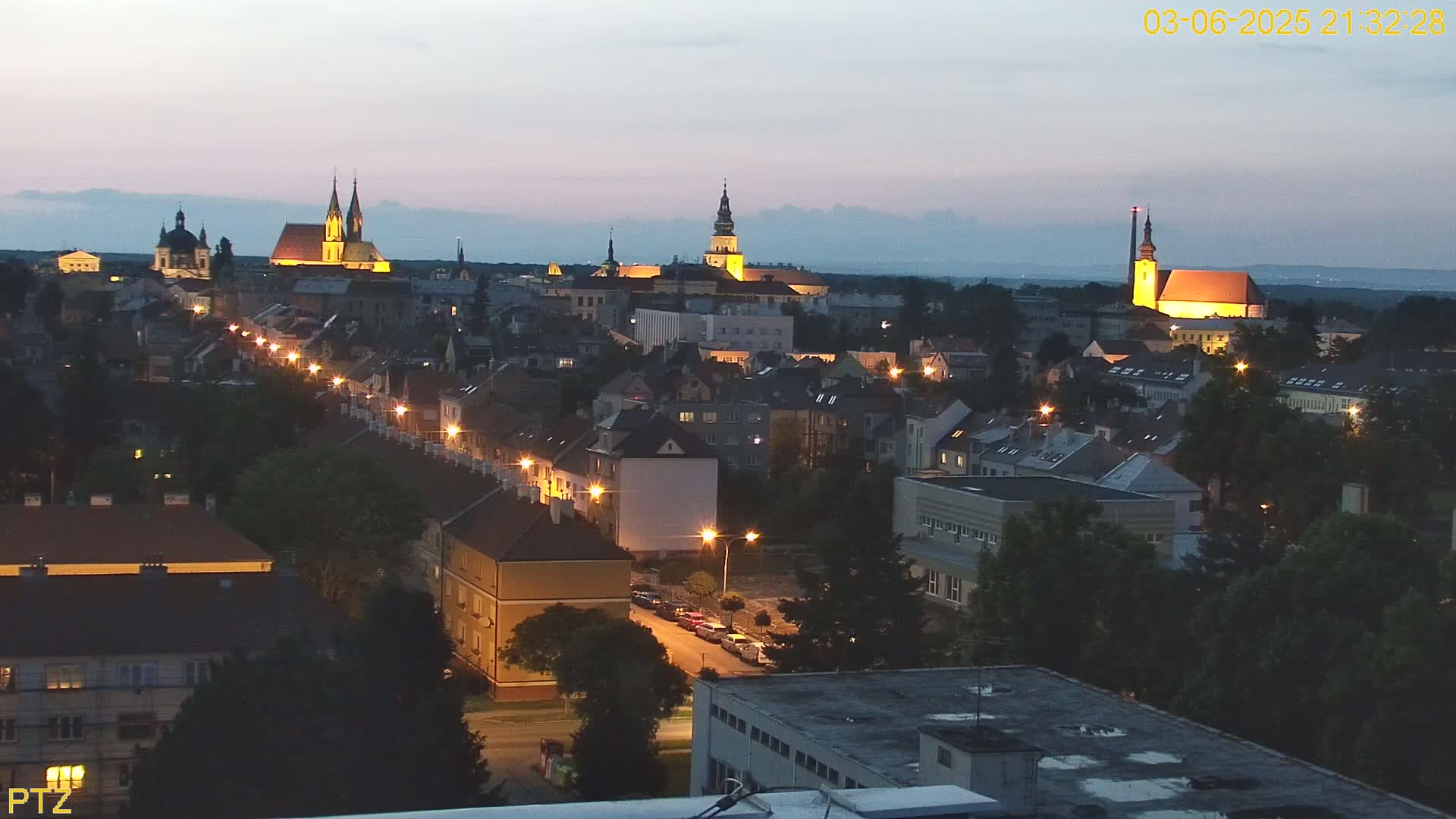 A nighttime view of a city illuminated by streetlights, featuring several prominent churches and buildings under a twilight sky.