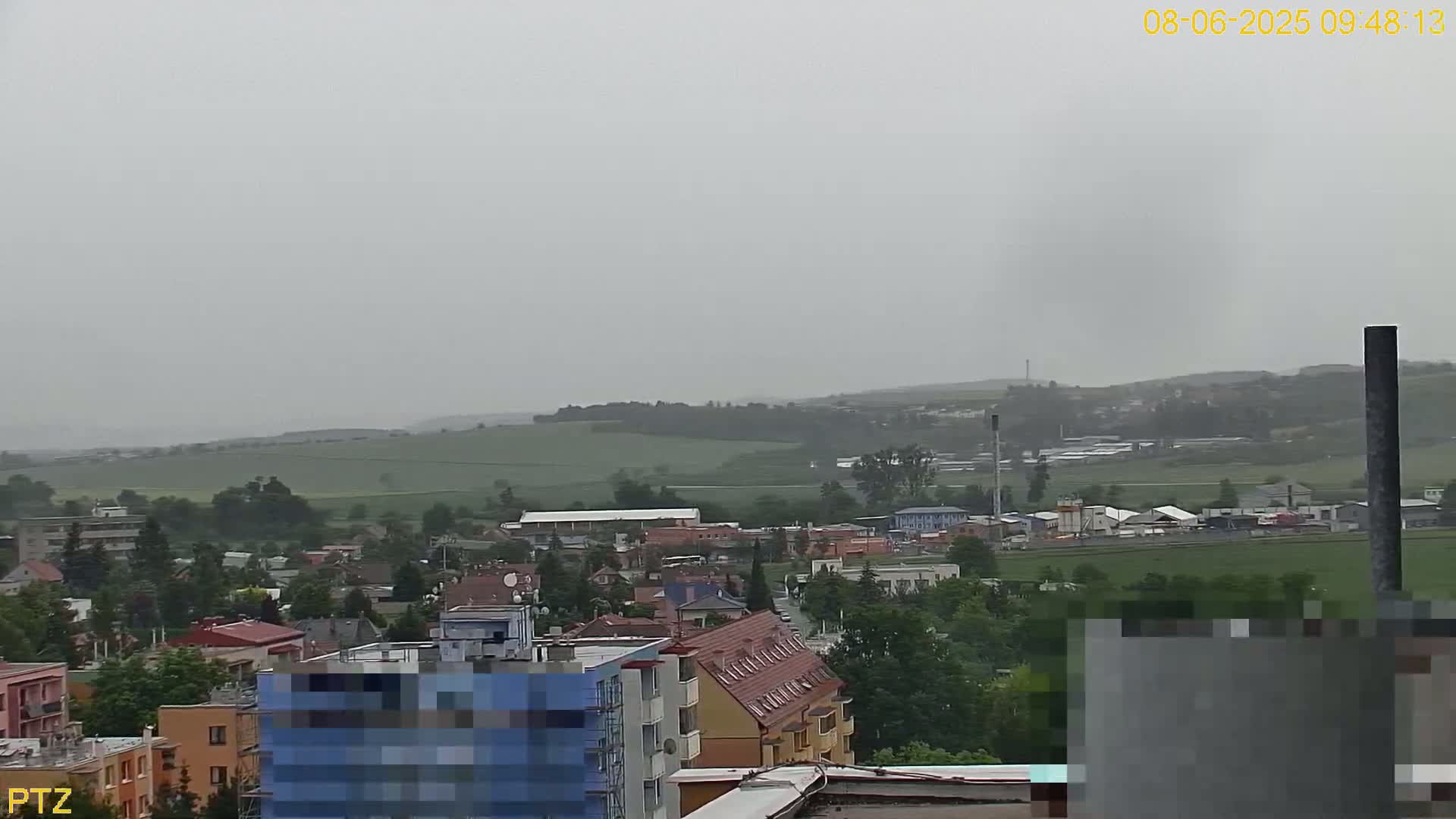 A hazy, overcast view shows a town nestled in a valley, with rolling green hills in the background.